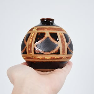 Puede incluir: Un jarrón pequeño, redondo, de cerámica marrón y negro con un diseño geométrico.