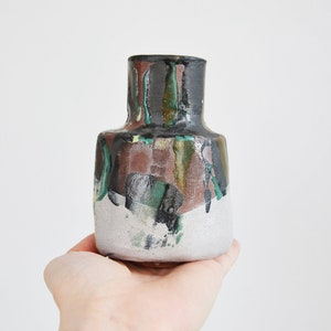 Può includere: Un piccolo vaso in ceramica dipinto a mano con una base bianca e disegni astratti in nero, verde e marrone.