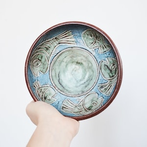 May include: A blue ceramic bowl with a brown rim and a design of white fish on the inside.