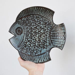 May include: A ceramic fish-shaped decorative plate with a teal and brown color scheme. The plate features intricate geometric patterns and a textured surface. The fish has an open mouth and detailed fins, perfect for home decor.