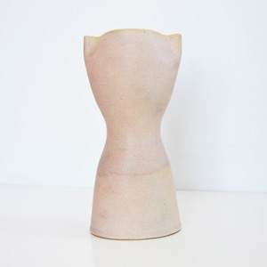 May include: A light pink ceramic vase with a unique hourglass shape and two small ear-like handles on the top.