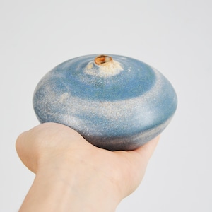 May include: A small, blue and white ceramic vase with a swirling pattern. The vase is being held in a hand.