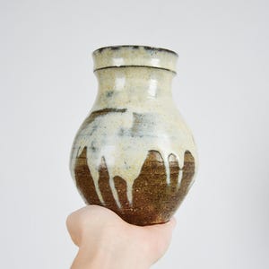 May include: A white ceramic vase with brown and black glaze, featuring a drip-like design. The vase has a rounded body and a slightly flared opening.