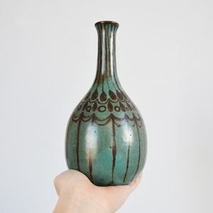 May include: A teal ceramic vase with a brown glaze and intricate design. The vase has a narrow neck and a rounded body.