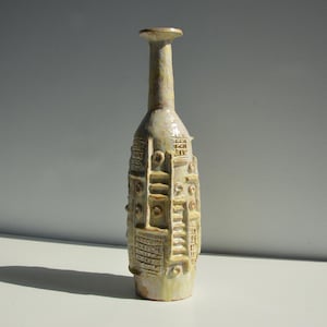 Könnte beinhalten: Eine weiße Keramikvase mit strukturierter Oberfläche und geometrischem Muster. Die Vase hat einen schmalen Hals und einen breiten Boden.