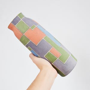 Könnte beinhalten: Eine Keramikvase mit einem geometrischen Muster in Grün-, Blau-, Lila- und Orangetönen. Die Vase ist handbemalt und hat ein einzigartiges, modernes Design.