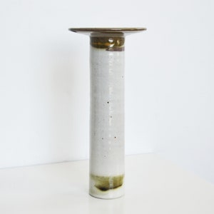 May include: A white ceramic vase with brown and green glaze accents. The vase has a wide, flat top and a cylindrical body.