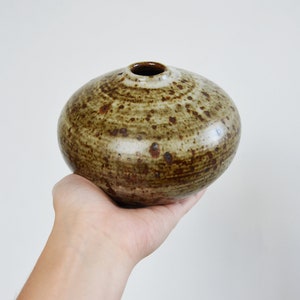 Könnte beinhalten: Eine kleine, runde Keramikvase mit einem gesprenkelten braunen und weißen Überzug.