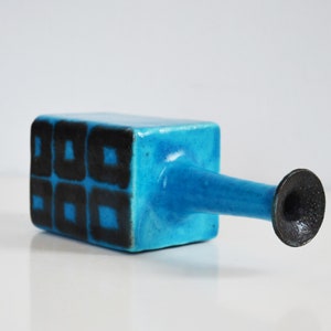 K&ouml;nnte beinhalten: Eine blaue Keramikvase mit geometrischem schwarzem Design. Die Vase hat einen quadratischen K&ouml;rper und einen langen, d&uuml;nnen Ausguss.