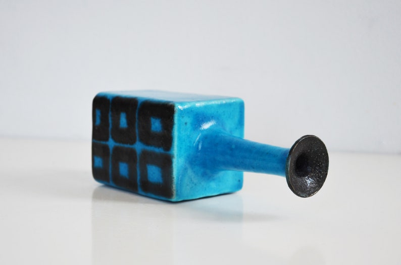 K&ouml;nnte beinhalten: Eine blaue Keramikvase mit geometrischem schwarzem Design. Die Vase hat einen quadratischen K&ouml;rper und einen langen, d&uuml;nnen Ausguss.