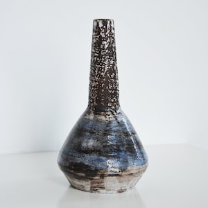 Puede incluir: Un jarrón de cerámica con un esmalte marrón y azul. El jarrón tiene un cuello estrecho y una base ancha y redondeada.