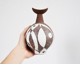 Może przedstawiać: Brązowy ceramiczny wazon z białym abstrakcyjnym wzorem. Wazon ma zaokrąglone ciało i krótki, zakrzywiony szyjkę.