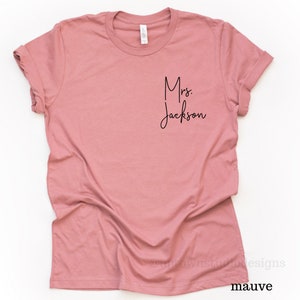 May include: Mauve colored t-shirt with the text "Mrs. Jackson" in black script font.