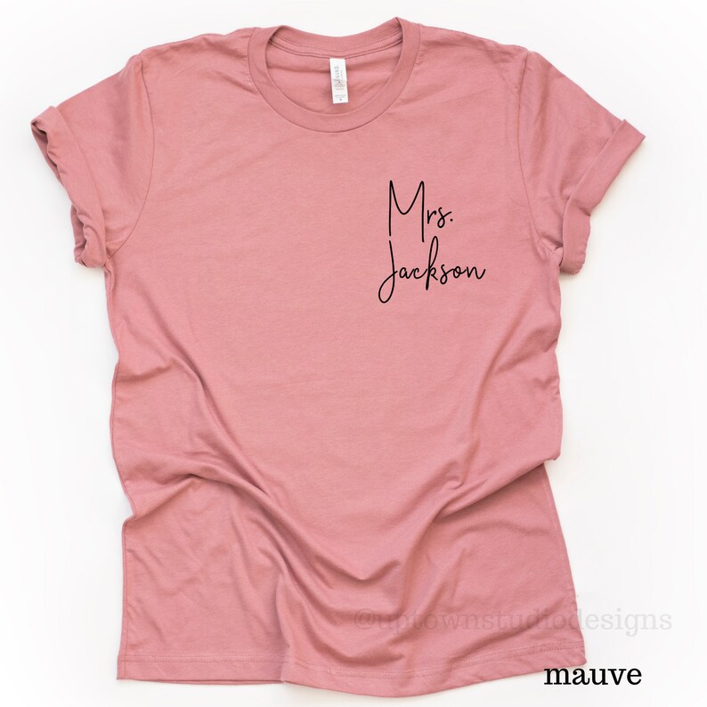 May include: Mauve colored t-shirt with the text "Mrs. Jackson" in black script font.