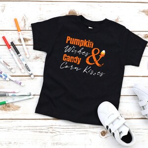 Puede incluir: Camiseta negra con un gráfico naranja que dice "Pumpkin Wishes & Candy Corn Kisses".