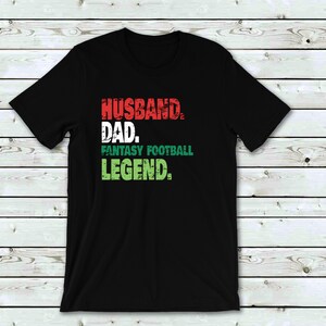 May include: Black t-shirt with a distressed graphic design that reads "Husband. Dad. Fantasy Football Legend."