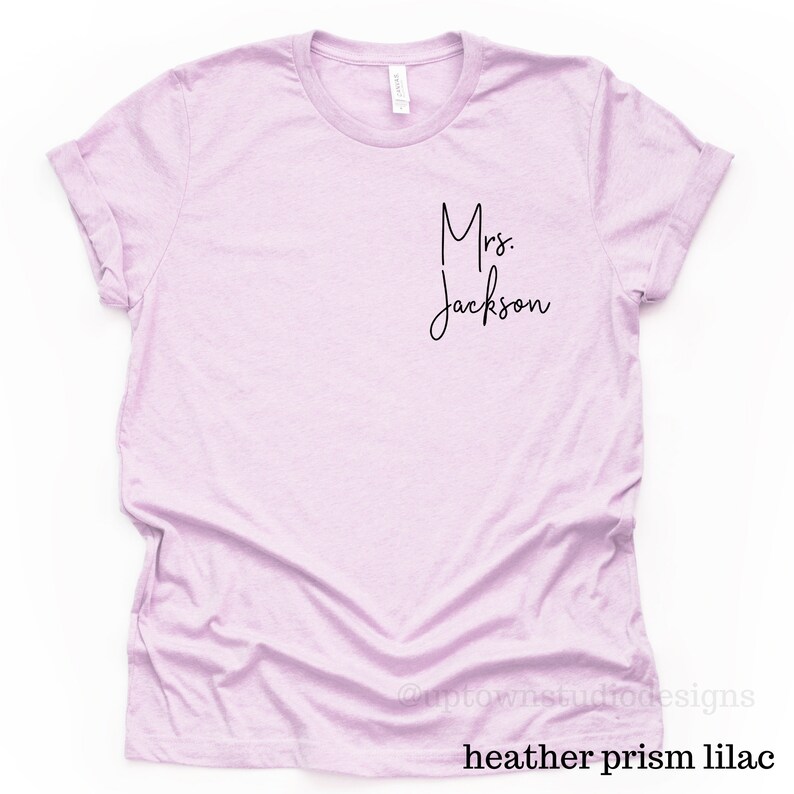 May include: A light purple t-shirt with the text "Mrs. Jackson" in black script.