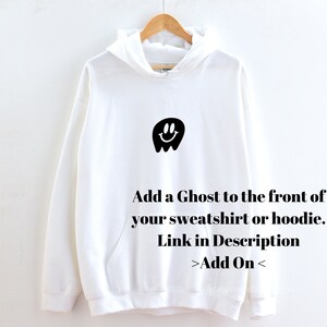 May include: White hooded sweatshirt with a black ghost graphic with a smiley face. The text "Add a Ghost to the front of your sweatshirt or hoodie. Link in Description >Add On<" is printed below the graphic.