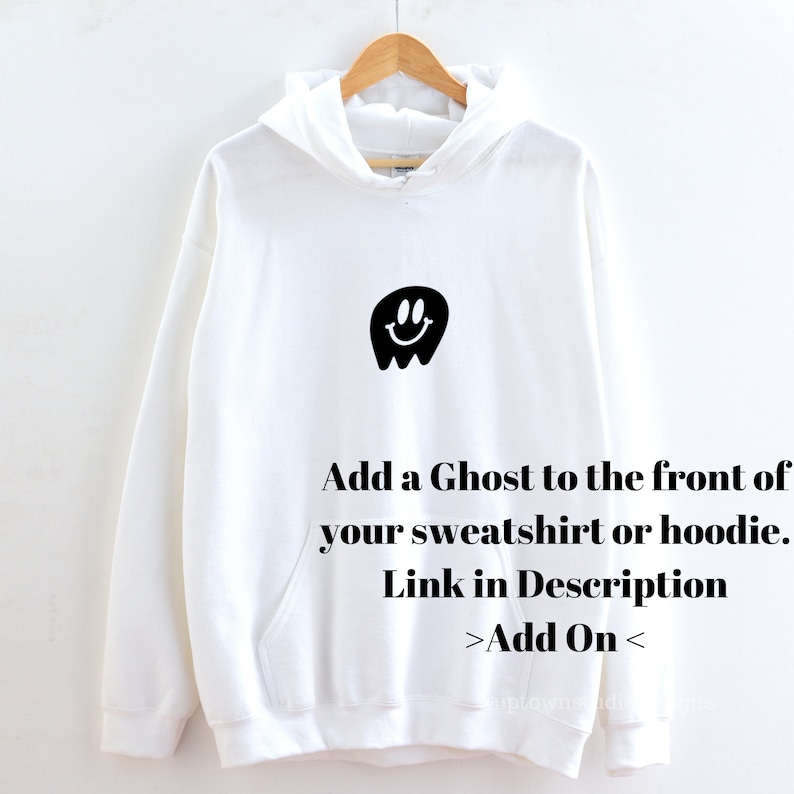 May include: White hooded sweatshirt with a black ghost graphic with a smiley face. The text "Add a Ghost to the front of your sweatshirt or hoodie. Link in Description >Add On<" is printed below the graphic.