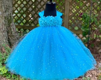 May include: A light blue tulle tutu dress with a flower embellishment around the bodice. The tulle is covered in silver glitter.