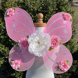 May include: Pink fairy wings with silver glitter and white, pink, and light pink flowers.