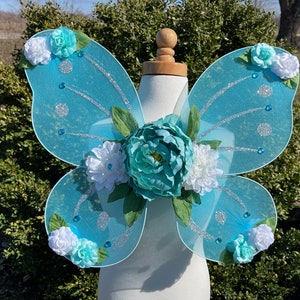 May include: Light blue fairy wings with white and teal flowers and glitter accents.