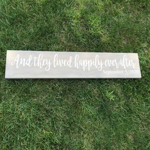 May include: A wooden sign with the text "And they lived happily ever after" in white cursive lettering. The date "September 5, 2020" is written in smaller white lettering below the main text.