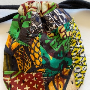 May include: A small drawstring bag made of patchwork fabric. The bag is made of different colorful fabrics with geometric patterns in shades of green, yellow, brown, and black.