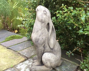 Könnte beinhalten: Eine graue Gartenstatue aus Beton, die ein sitzendes Kaninchen mit hochgestellten Ohren darstellt, das nach oben schaut.
