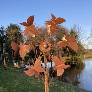 May include: A rusty metal garden sculpture of a flower with six butterfly wings. The sculpture is in a garden setting with a pond in the background.