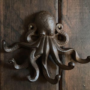 May include: A cast iron octopus wall hook with eight tentacles, each ending in a hook. The octopus is painted in a dark brown colour and has a rustic finish.