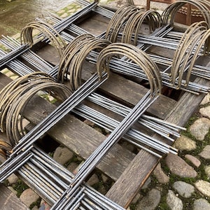 May include: A stack of metal garden hoops, arranged on a wooden pallet. The hoops are made of thin, silver-coloured metal and are designed to support plants.