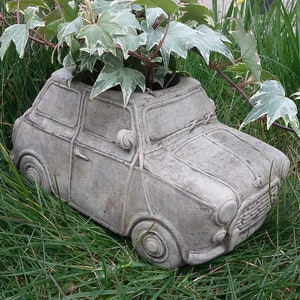 May include: A grey concrete car-shaped planter, planted with green and white variegated ivy. The planter is set in green grass, a charming garden feature. The planter is a miniature car.