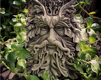 May include: A grey stone sculpture of a Green Man's face, surrounded by leaves and vines. The sculpture is detailed with a beard, moustache, and eyes.