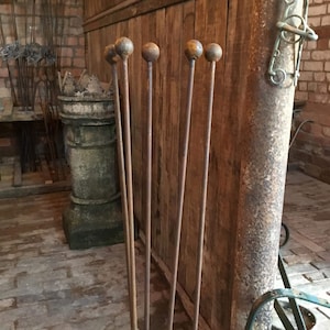 May include: A set of six rusty metal garden stakes with rounded tops. The stakes are arranged in a row against a wooden wall.