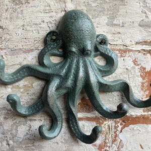 May include: A green cast iron octopus wall hook with eight tentacles that are shaped like hooks. The octopus is mounted on a brick wall.