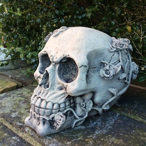 May include: A white concrete skull with roses sculpted into the bone. The skull is sitting on a brick surface.