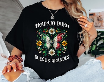 Könnte beinhalten: Schwarzes T-Shirt mit einem Schmetterlingsdesign in den Farben der mexikanischen Flagge, umgeben von Blumen und Blättern. Der Text "TRABAJO DURO SUEÑOS GRANDES" ist oberhalb und unterhalb des Schmetterlings aufgedruckt.