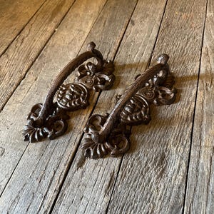 May include: Two ornate cast iron drawer pulls with a dark brown finish. The pulls have a decorative scroll design and are perfect for adding a touch of vintage charm to any furniture piece.