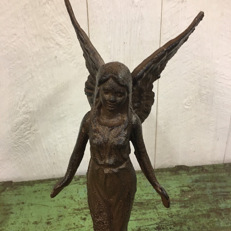 May include: A cast iron angel statue with wings outstretched. The angel is standing on a green surface and has a brown patina.