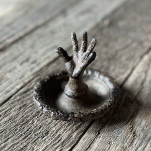 May include: A black metal ring holder shaped like a hand reaching up from a circular base.