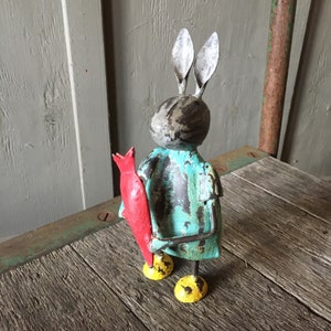 May include: A turquoise blue metal rabbit figurine holding a red metal fish. The rabbit has black and white paint details and yellow painted feet.