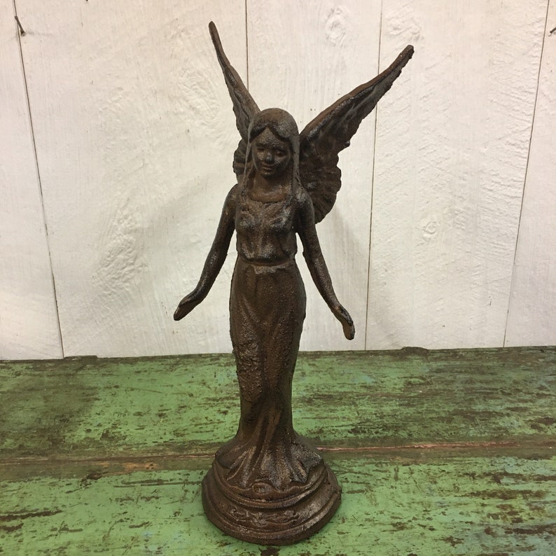 May include: A cast iron angel statue with wings outstretched, standing on a pedestal. The angel is painted in a dark brown color with a rustic finish.