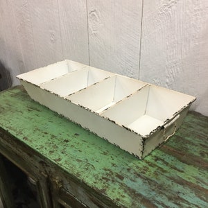 May include: White metal tray with four divided sections. The tray has a distressed finish and is perfect for organizing small items.