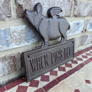 May include: A cast iron sign with a pig with wings and the text "When Pigs Fly".