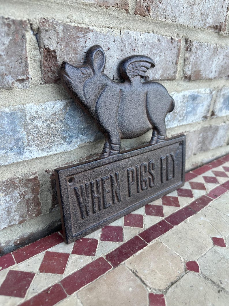 May include: A cast iron sign with a pig with wings and the text "When Pigs Fly".