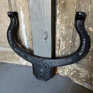 May include: Black cast iron U-shaped bracket with the text "AMERICAN CASTING CO BIRMINGHAM ALABAMA" and three holes.