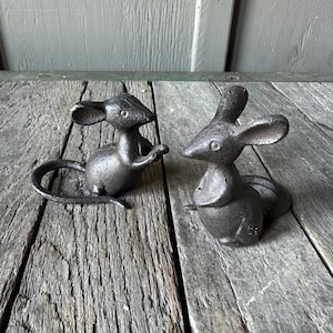 May include: Two black cast iron mouse figurines. The mice are sitting on a wooden surface.
