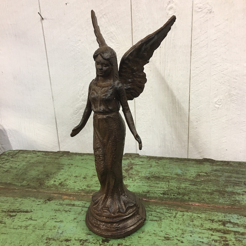 May include: A cast iron angel statue with wings outstretched. The angel is standing on a round base and is painted in a dark brown color.