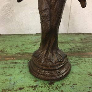 May include: A dark brown cast iron bird sculpture with intricate details. The bird is perched on a base with a decorative design.